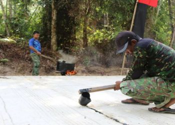 Anggota Satgas TMMD Lapisi Sambungan Semenisasi Jalan dengan Cairan Aspal
